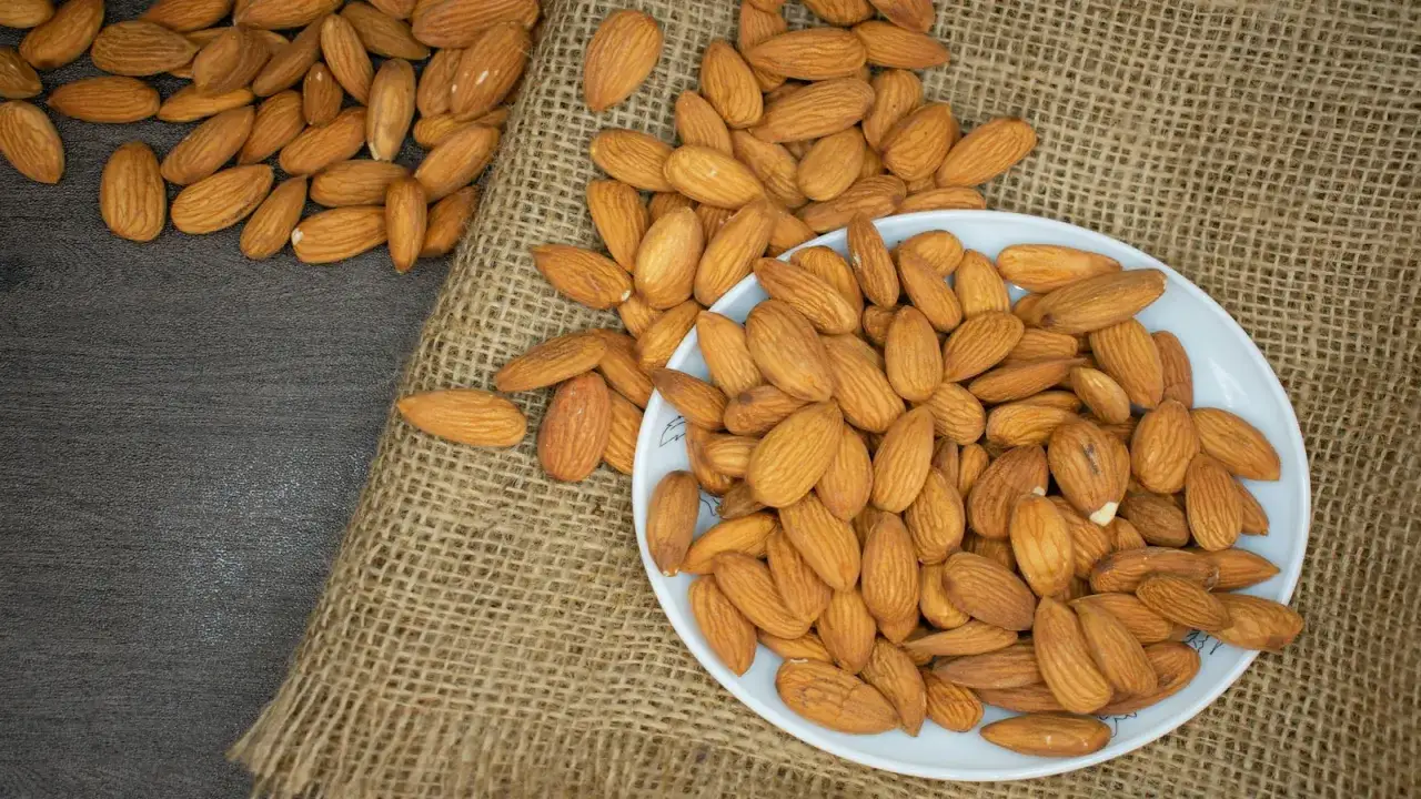 Migdały na talerzyku i obok, na płótnie. Niska zawartość cukru i niski indeks glikemiczny sprawiają, że są idealną przekąską.