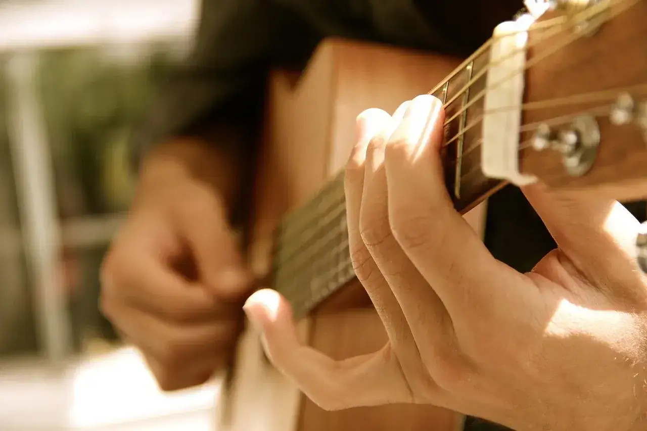 Dłonie grają na gitarze, tworząc melodyjny bas głos. Słońce oświetla palce, które zręcznie poruszają się po strunach.