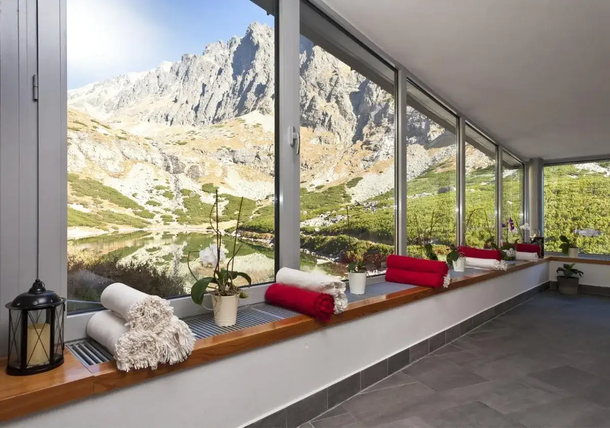 Relaks w schronisku Tatry z widokiem na g&oacute;ry i jezioro. Ręczniki i kwiaty na parapecie.
