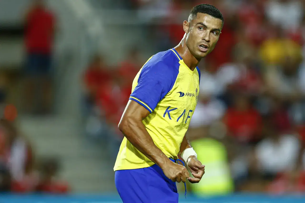 Piłkarz Cristiano Ronaldo w ż&oacute;łtej koszulce z niebieskimi rękawami, skupiony na boisku. Jego zarobki tygodniowe piłkarzy budzą podziw.