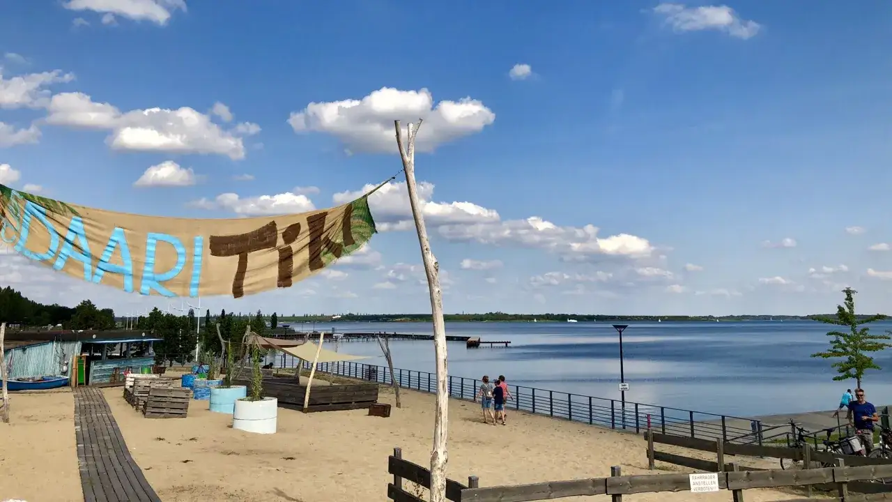 Sonniger Tag am Muldestausee. Menschen genießen das Baden und die Strandatmosphäre. Ein Banner mit der Aufschrift