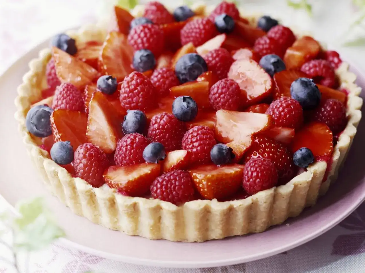 Ein **schneller Kuchen ohne Backen** mit frischen Erdbeeren, Himbeeren und Blaubeeren auf einem knusprigen Boden. Perfekt für heiße Tage!