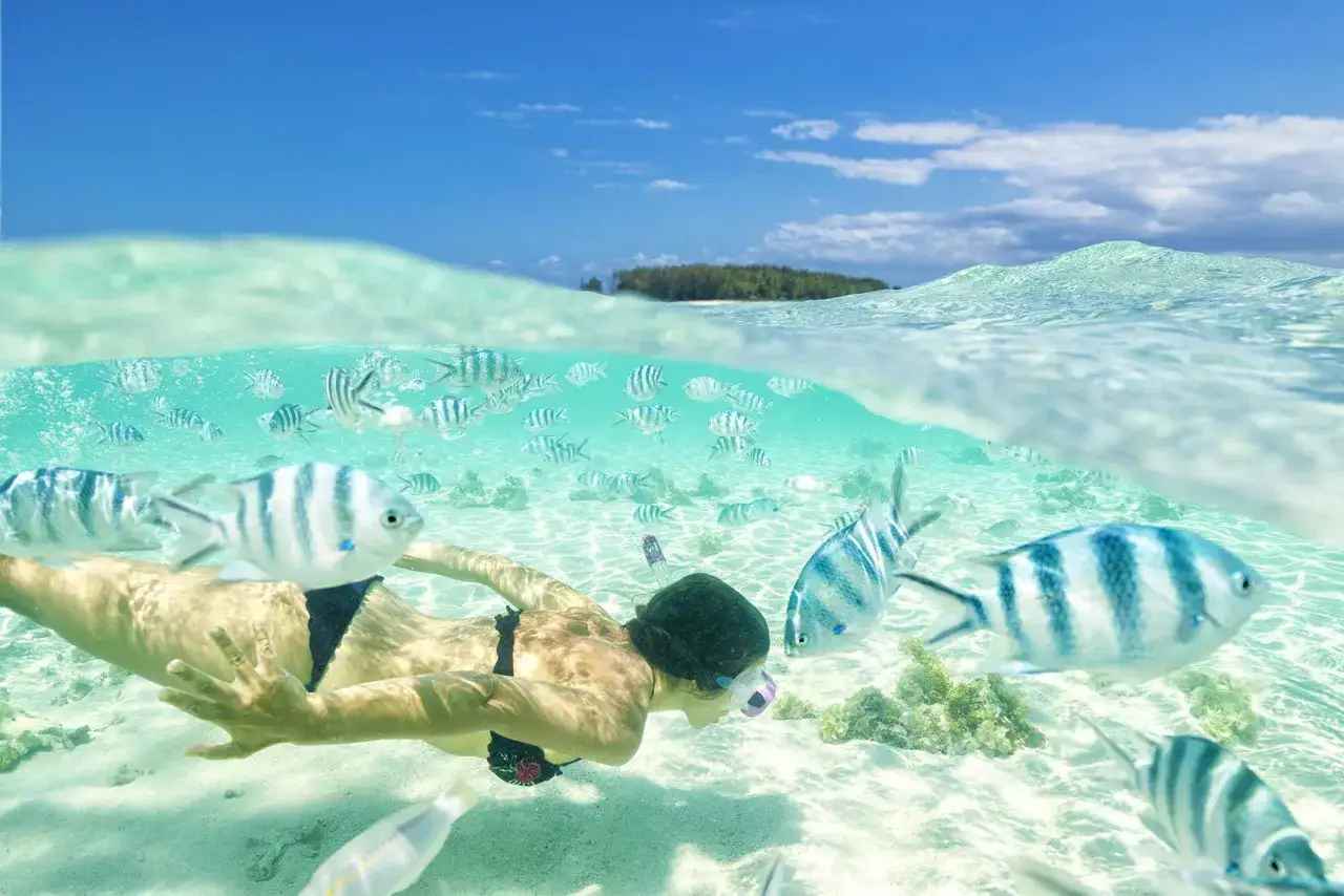Kobieta pływa z rybami w turkusowej wodzie. Idealna pogoda na Zanzibarze w październiku do snorkelingu.