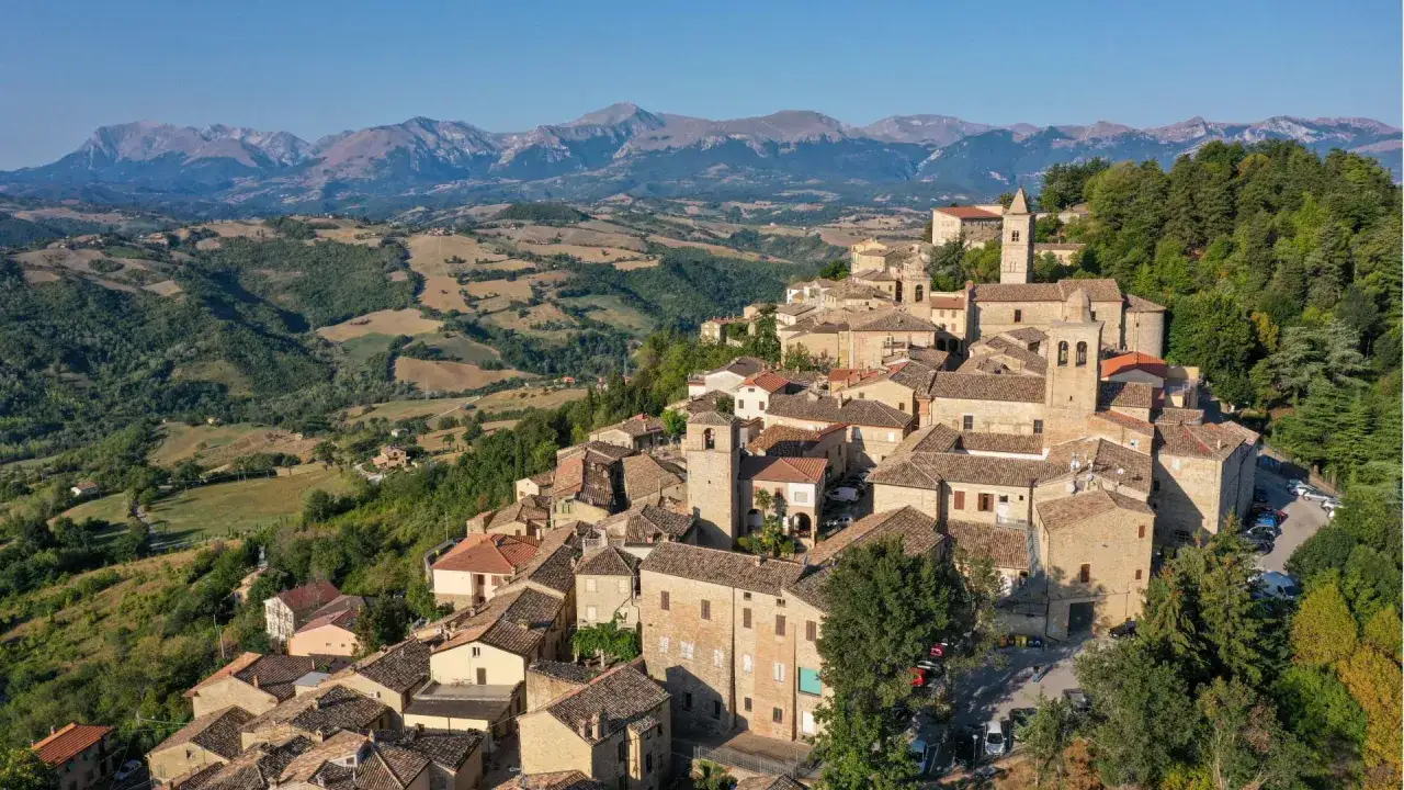 Borgo medievale di Penna San Giovanni, con case in pietra e tetti in cotto, incastonato tra dolci colline e montagne maestose.