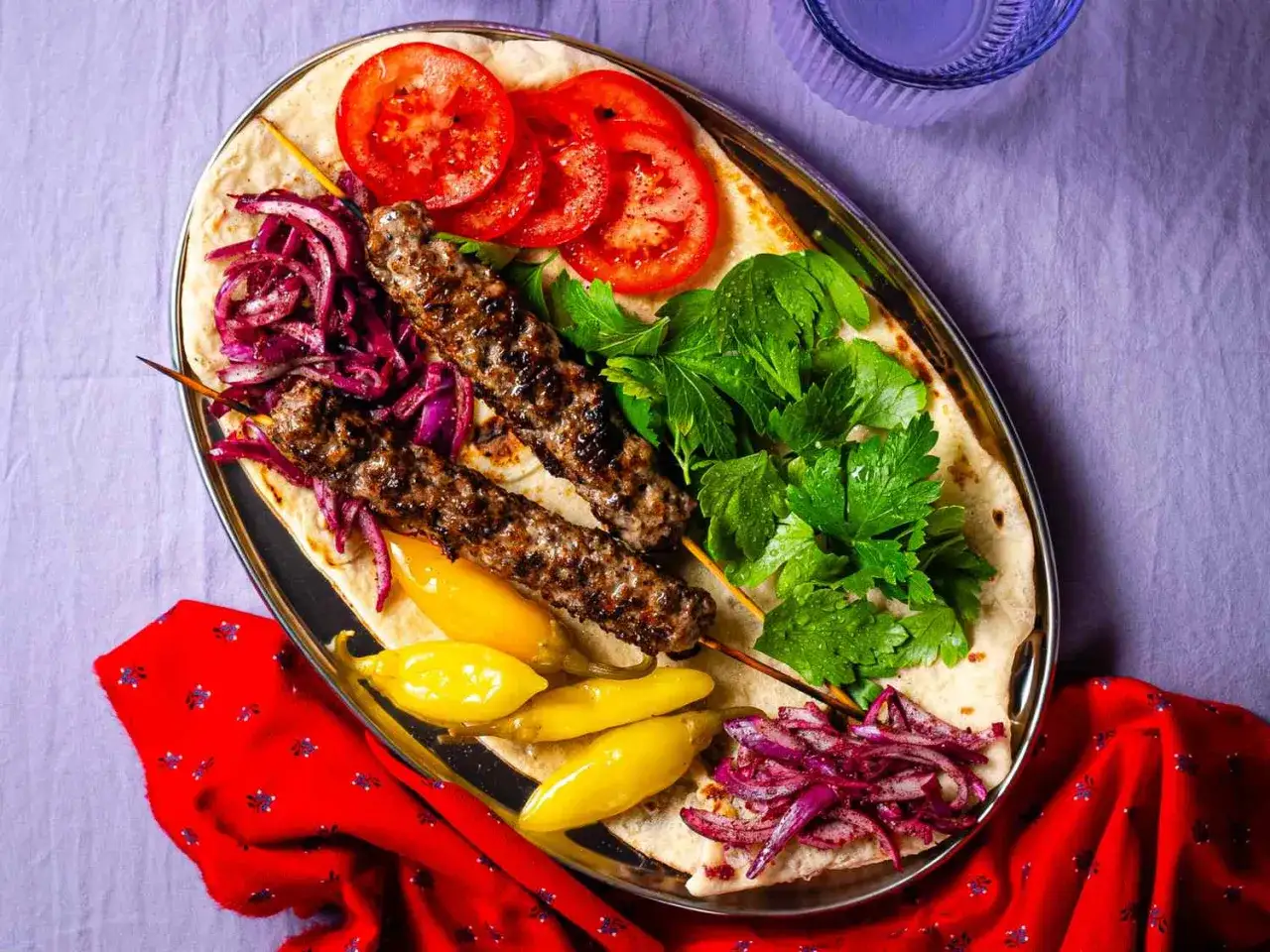 Adana kebab recept: grillade köttfärsspett med tomat, lök, persilja och chili på tunnbröd.