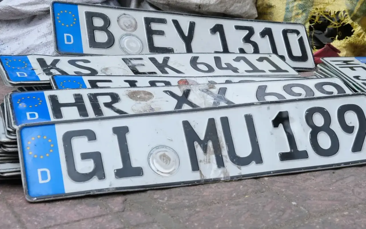 Stos niemieckich tablic rejestracyjnych, gotowych do rejestracji samochodu z Niemiec. Widać numery takie jak B EY 1310, KS EK 6411, HR XX 699, GI MU 189.