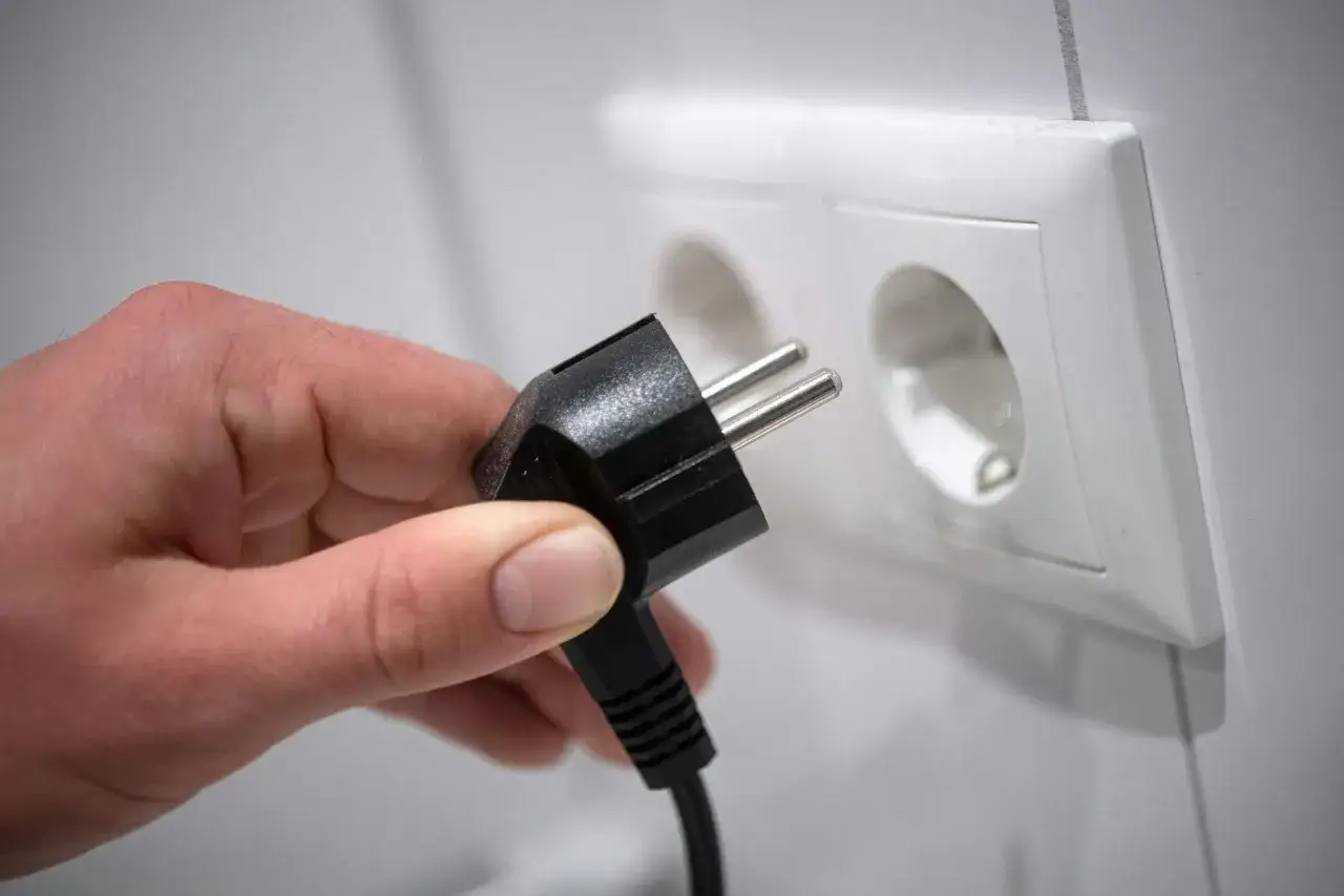 Hand h&auml;lt Stecker, um eine schmutzige Steckdose zu reinigen. Vorsicht bei der Steckdose reinigen!