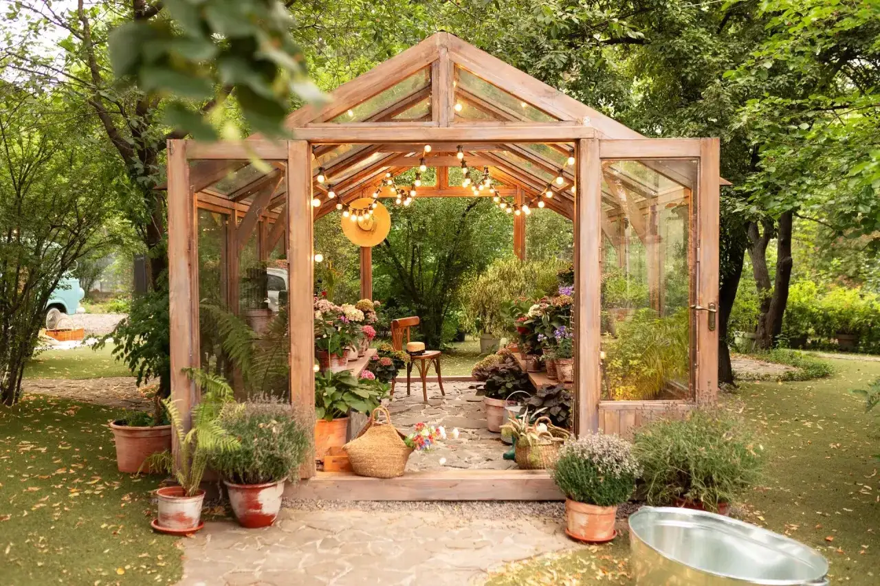 Une serre en bois, décorée de guirlandes lumineuses, invite à la détente. Un coin cocooning dans le jardin, avec des plantes et un fauteuil.
