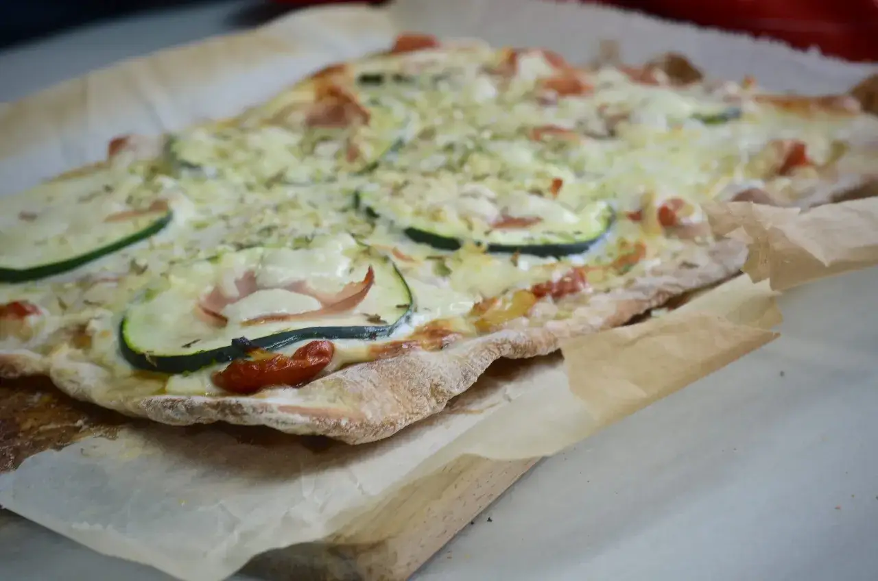 Pan pizza reci&eacute;n horneada con calabac&iacute;n, tomate y jam&oacute;n, sobre papel de horno.
