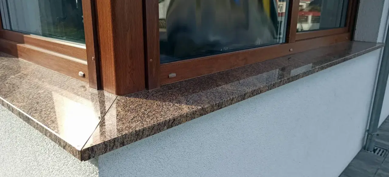 Eleganckie parapety kamienne w brązowo-beżowe wzory, idealnie komponują się z drewnianą ramą okna, dodając klasy.
