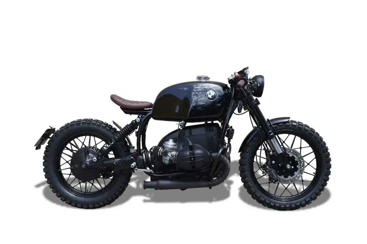 Elegante moto tipo scrambler negra, con asiento marr&oacute;n y neum&aacute;ticos todoterreno, lista para la aventura.
