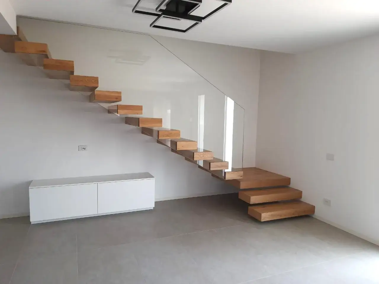 Moderna scala a sbalzo in legno, ottima tra le idee per soppalco in legno, con parapetto in vetro e mobile bianco.
