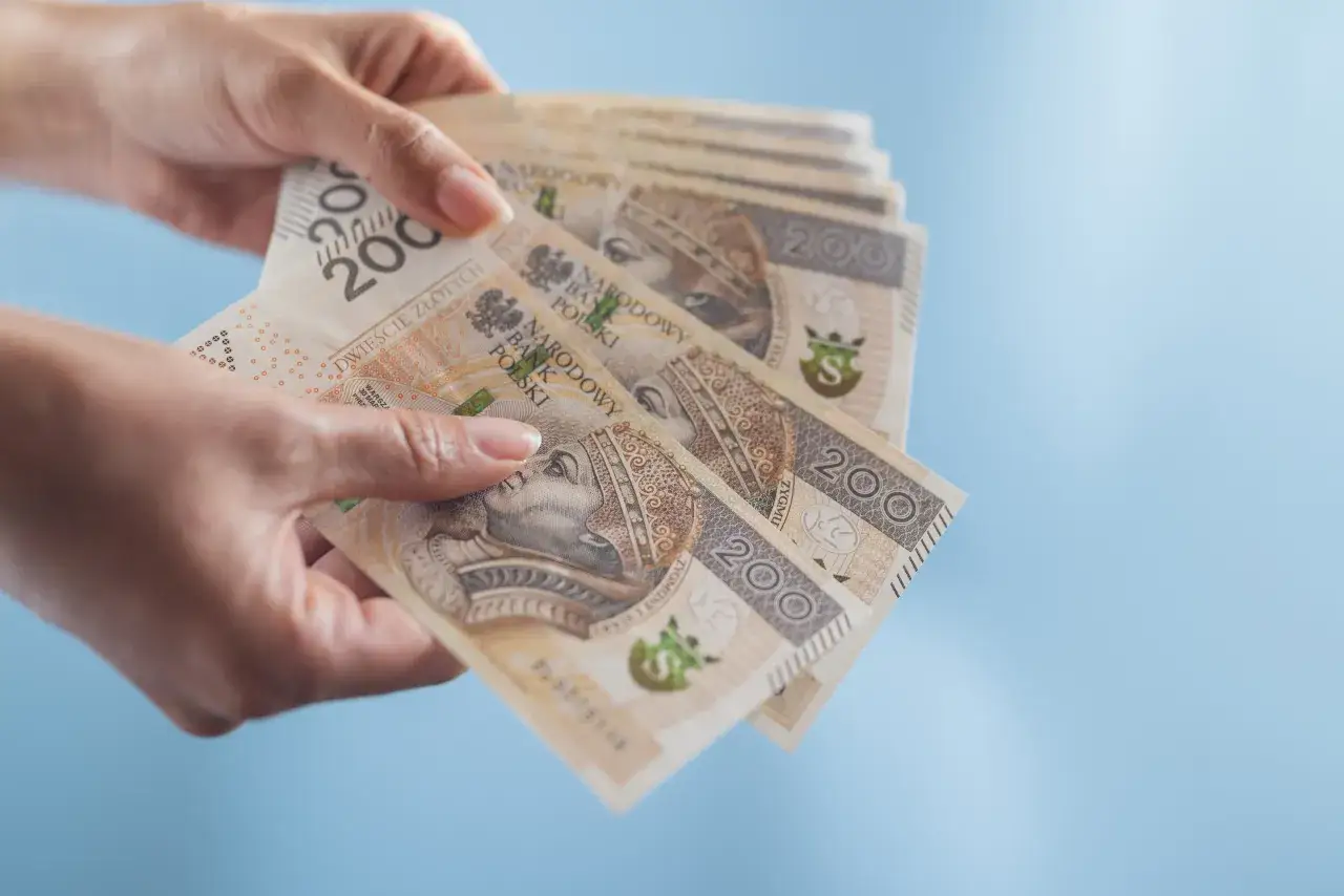 Dłonie trzymają stos banknotów 200 zł. Dowiedz się, jak wziąć pożyczkę na dowód, gdy potrzebujesz gotówki.