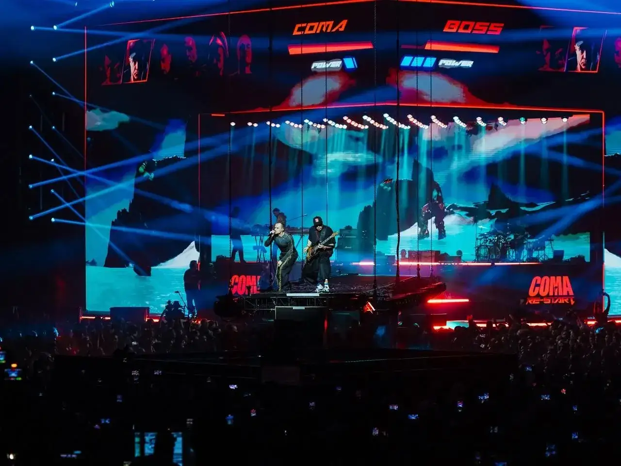 Energetyczne **coma koncerty 2025** na żywo! Wokalista i gitarzysta na scenie, tłum szaleje, a ekran rozświetla grafikę.