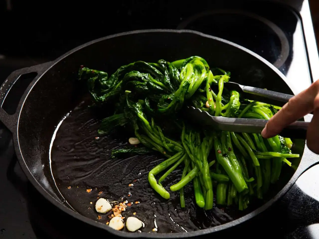 Verduras verdes se rehogan en sartén de hierro fundido con ajo.