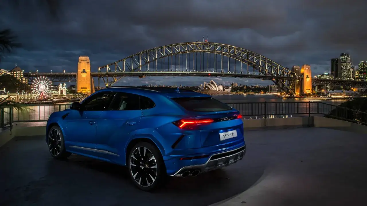 Niebieski Lamborghini Urus na tle nocnego Sydney z mostem i Operą.
