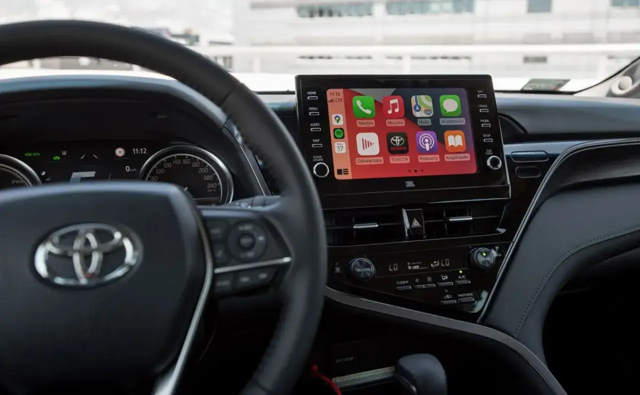 Wnętrze Camry 2024 z ekranem multimedialnym Apple CarPlay, kierownicą i zegarami.