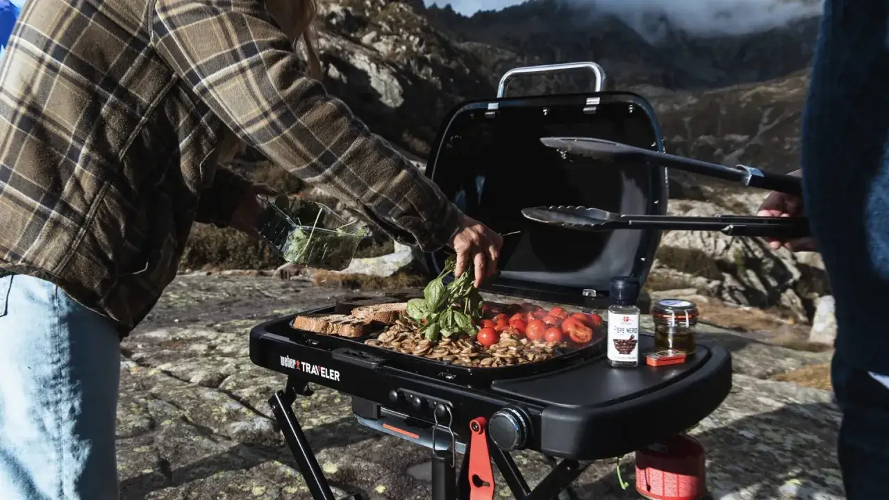 En person l&auml;gger f&auml;rska &ouml;rter p&aring; en **weber liten grill** med tomater och svamp i bergen.