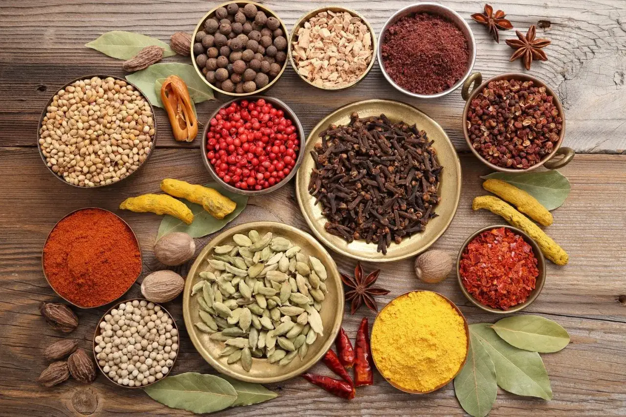 En samling kryddor som korianderfrön, kardemumma, nejlikor och gurkmeja. Perfekt för att skapa en smakrik **masala krydda**.
