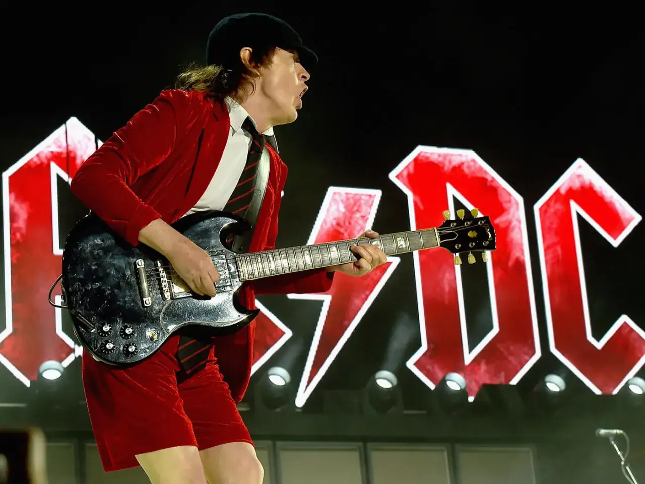 Angus Young w czerwonym stroju gra na gitarze, a za nim logo AC/DC. To pewnie koncert z największe przeboje!