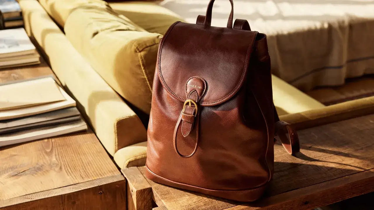 Sac &agrave; dos en cuir v&eacute;g&eacute;tal marron, pos&eacute; sur une table en bois, &agrave; c&ocirc;t&eacute; d'un canap&eacute;.