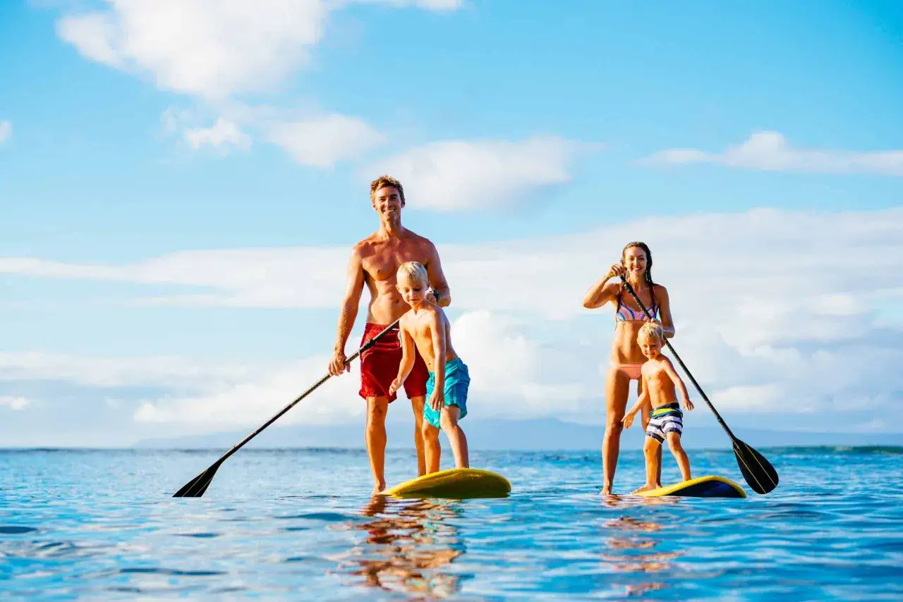Rodzina cieszy się słońcem i wodą, uprawiając sporty wodne po angielsku - paddleboarding na spokojnym morzu.