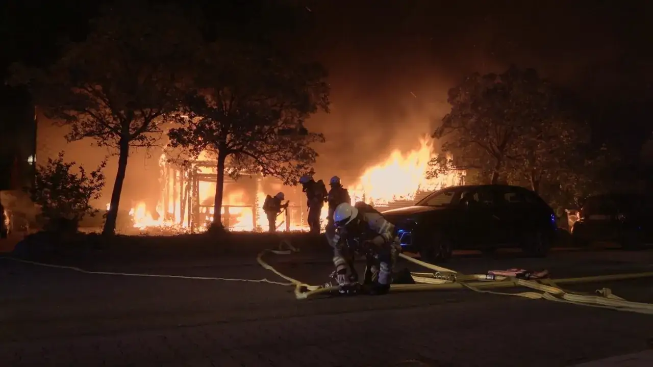 Feuerwehrleute kämpfen gegen einen Großbrand, der ein Gebäude in Flammen aufgehen lässt. Die Szene erinnert an