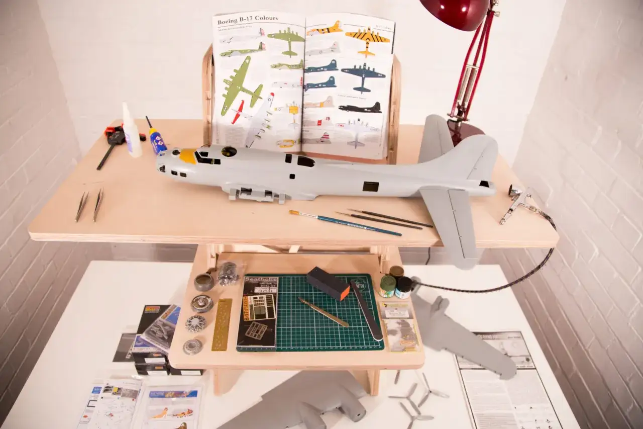 Detailreicher **Plastikmodellbau** eines Flugzeugs, mit Werkzeugen, Farben und einem Referenzbuch.