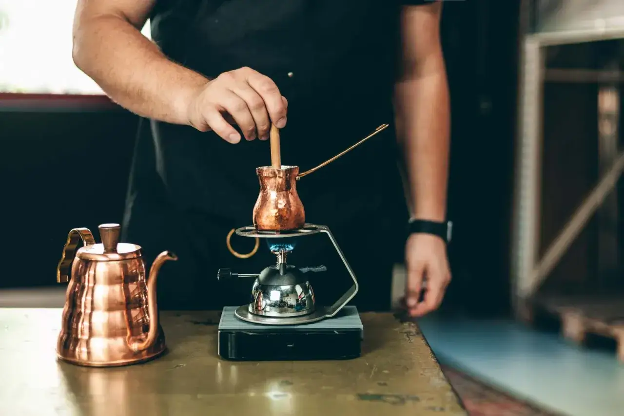 Barista bereitet t&uuml;rkischen Mokka auf einem kleinen Brenner zu. Daneben steht eine kupferne Kaffeekanne.