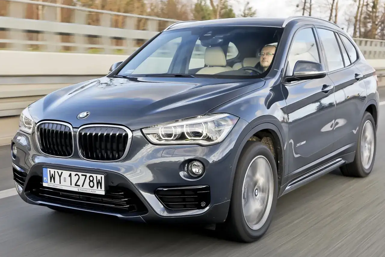 Szary BMW X1 w ruchu drogowym. Kierowca w okularach. Zastanawiasz się, ile kosztuje BMW X1?