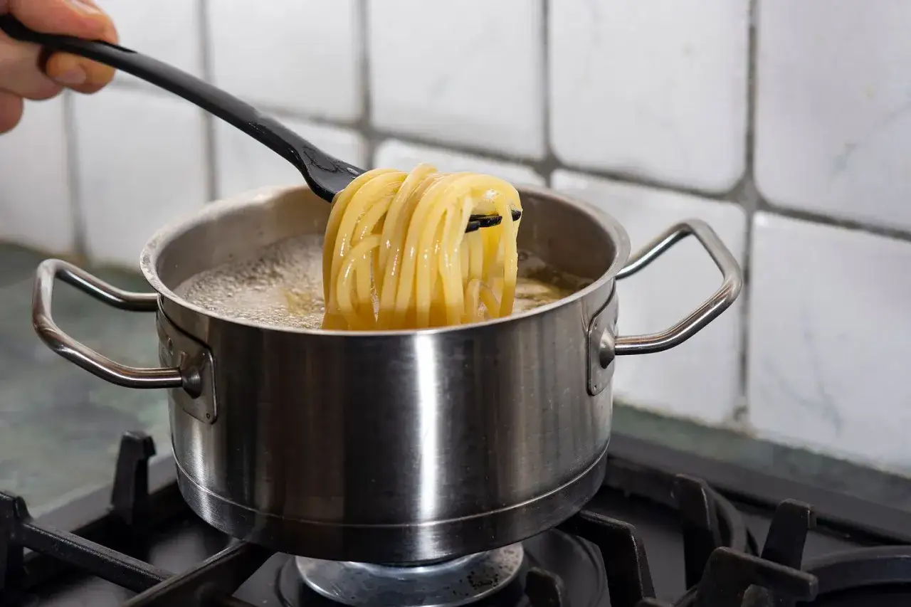 Łyżka podnosi z garnka idealny makaron al dente, gotujący się w bulgoczącej wodzie.
