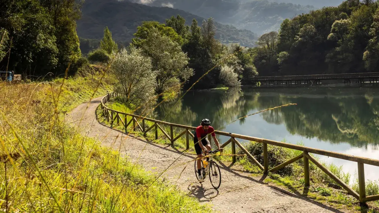 Ciclista en una vía verde, disfrutando de un paisaje idílico junto a un lago. Un ejemplo de las mejores vías verdes España.