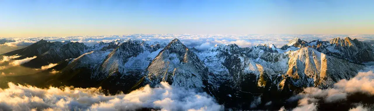 Majestatyczne Tatry Wysokie o wschodzie słońca, z chmurami otulającymi zbocza. W oddali widać Gerlach, najwyższy szczyt Słowacji.