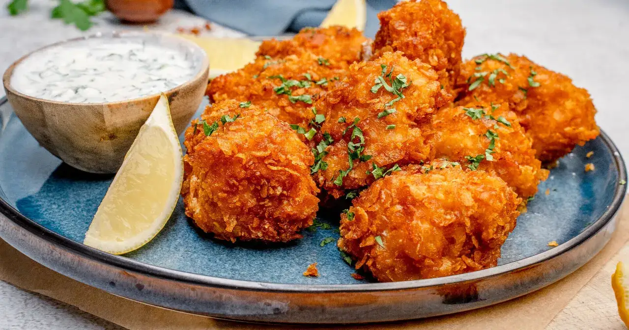 Knusprige chicken nuggets, frisch aus der Fritteuse, garniert mit Petersilie, serviert mit Dip und Zitronenspalten.