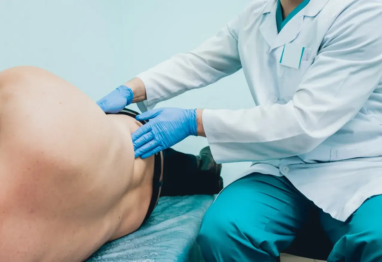 Lekarz w rękawiczkach wykonuje badanie urologiczne mężczyzn, palpacyjnie oceniając okolice brzucha.
