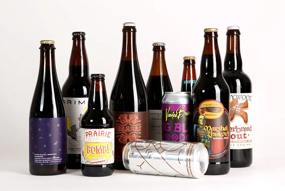 Una selezione di birre scure, tra cui una birra stout, in bottiglie e lattine su sfondo bianco.