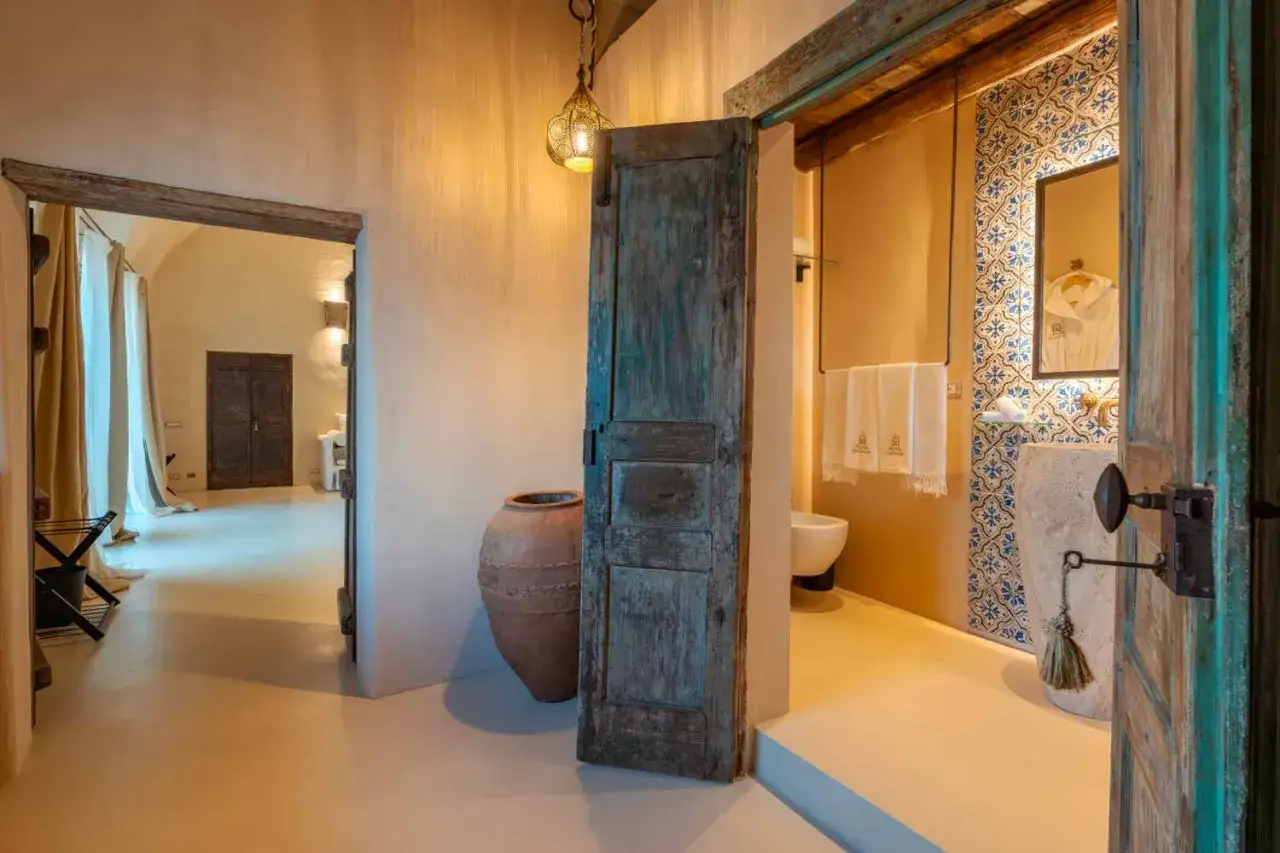 Un bagno con pavimenti in resina, un'antica porta in legno e un vaso di terracotta.