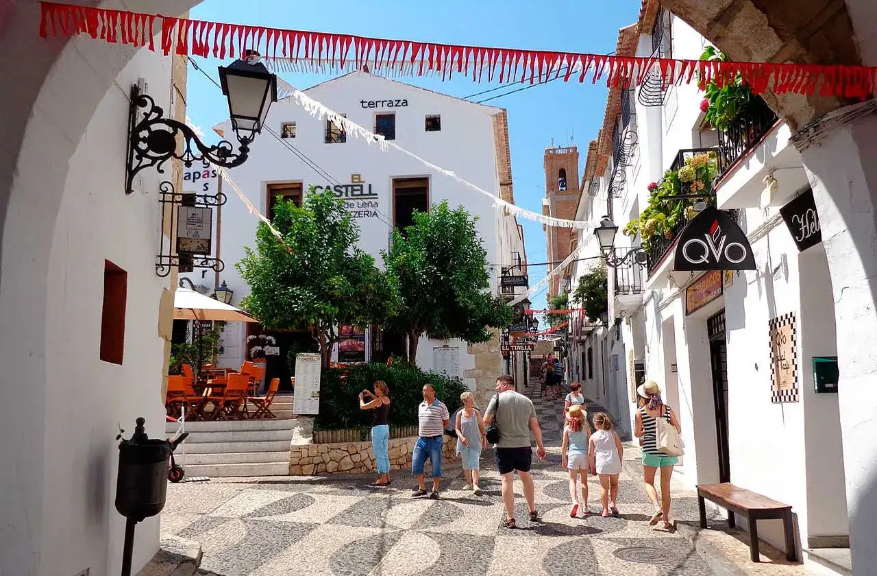 Calle empedrada con gente paseando, un caf&eacute; y un restaurante. Un ejemplo de los pueblos m&aacute;s bonitos de Alicante.