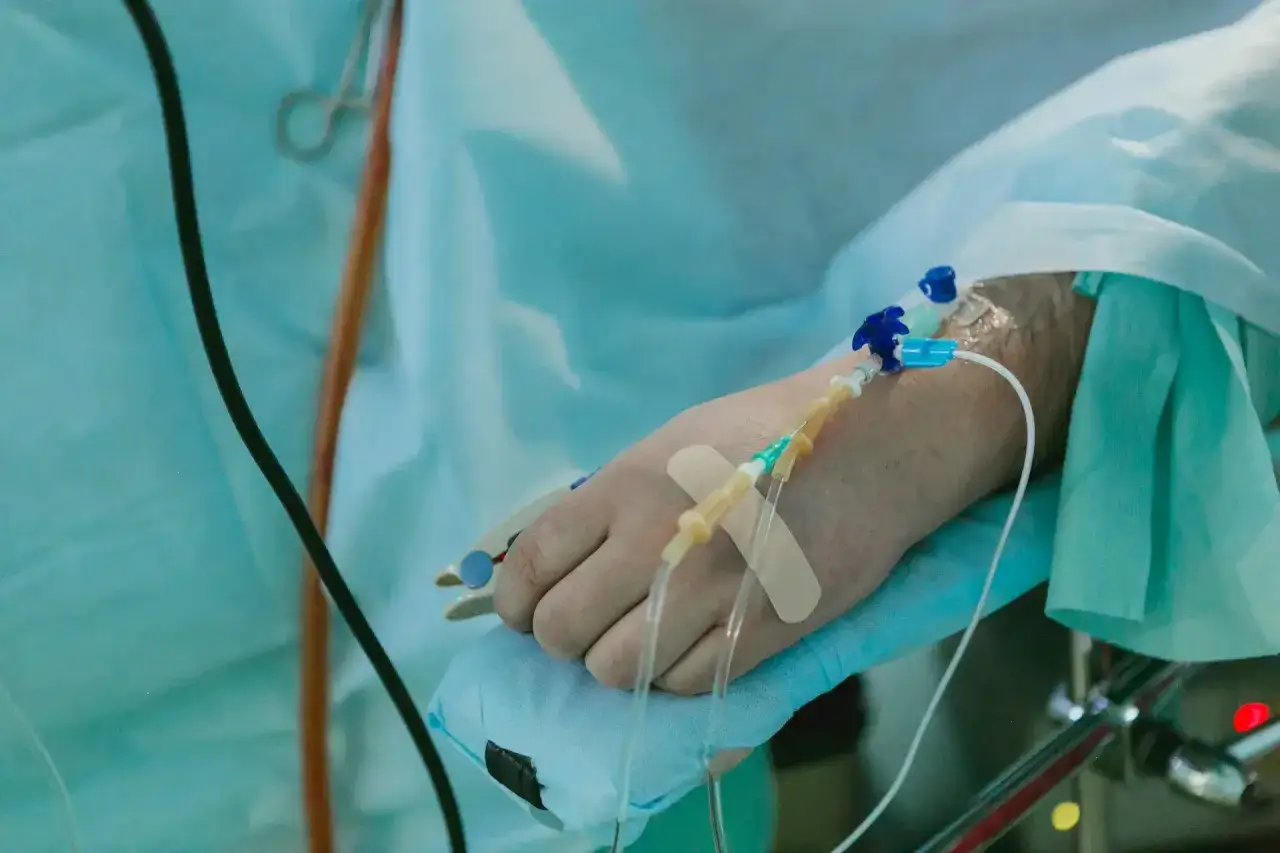 Ręka pacjenta z wenflonem i plastrem, przygotowana do podawania płyn&oacute;w po operacji.