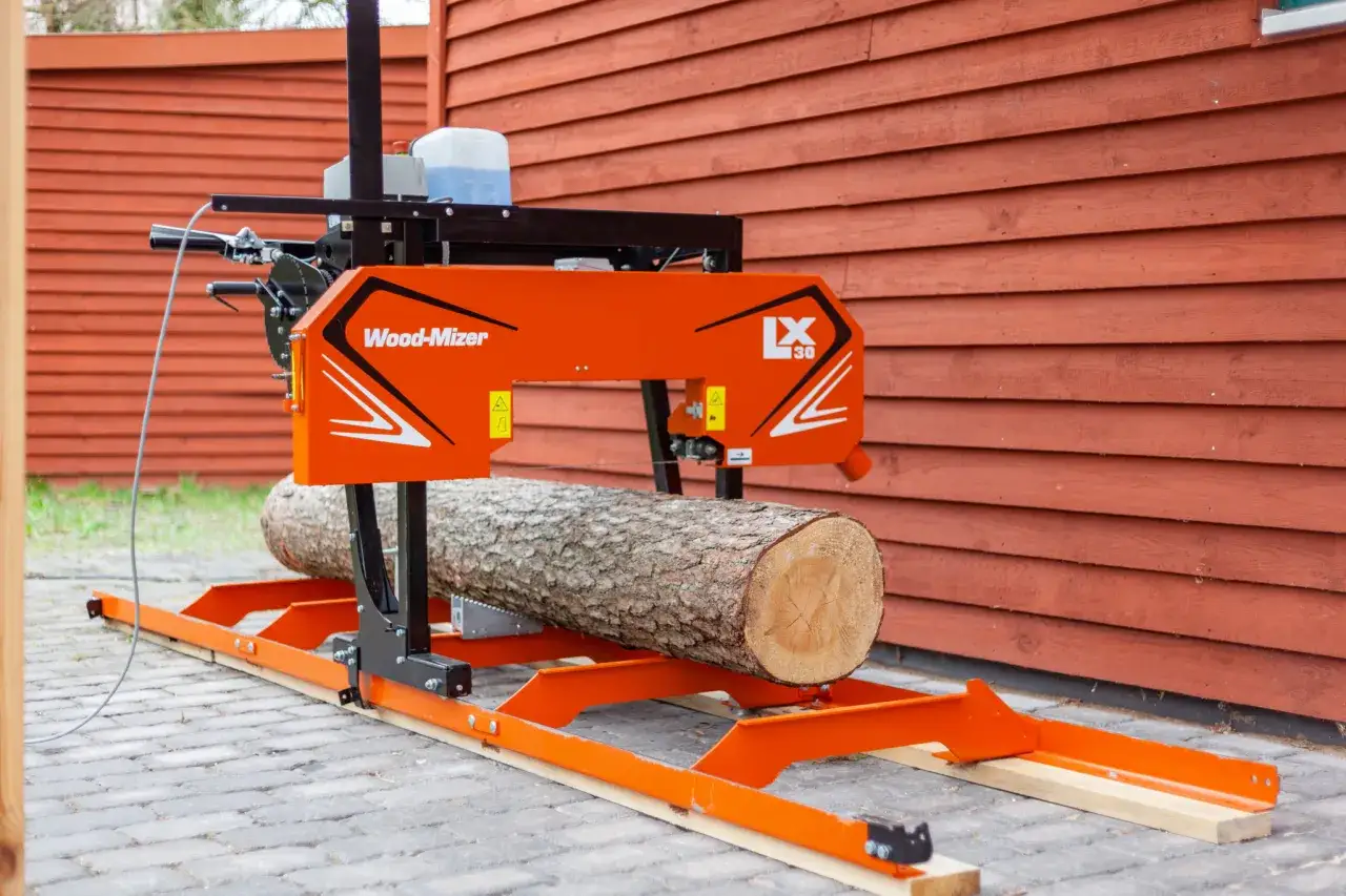 Pomarańczowa piła Wood-Mizer LX30 gotowa do cięcia drewna na deski. Kłoda leży na ramie, czekając na precyzyjne cięcie.