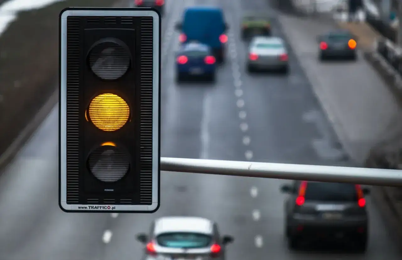 Sygnalizacja świetlna pokazuje żółte światło, ostrzegając kierowców przed zbliżającym się czerwonym. Samochody na drodze przygotowują się do zatrzymania.