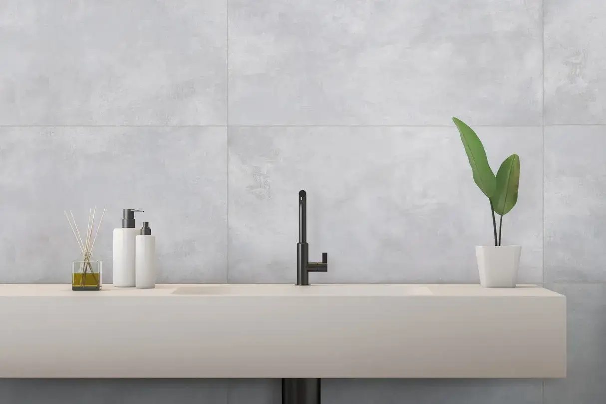 &Eacute;l&eacute;gant lavabo avec robinetterie noire, flacons de savon et plante verte, sur un mur en carrelage rectifi&eacute; gris.