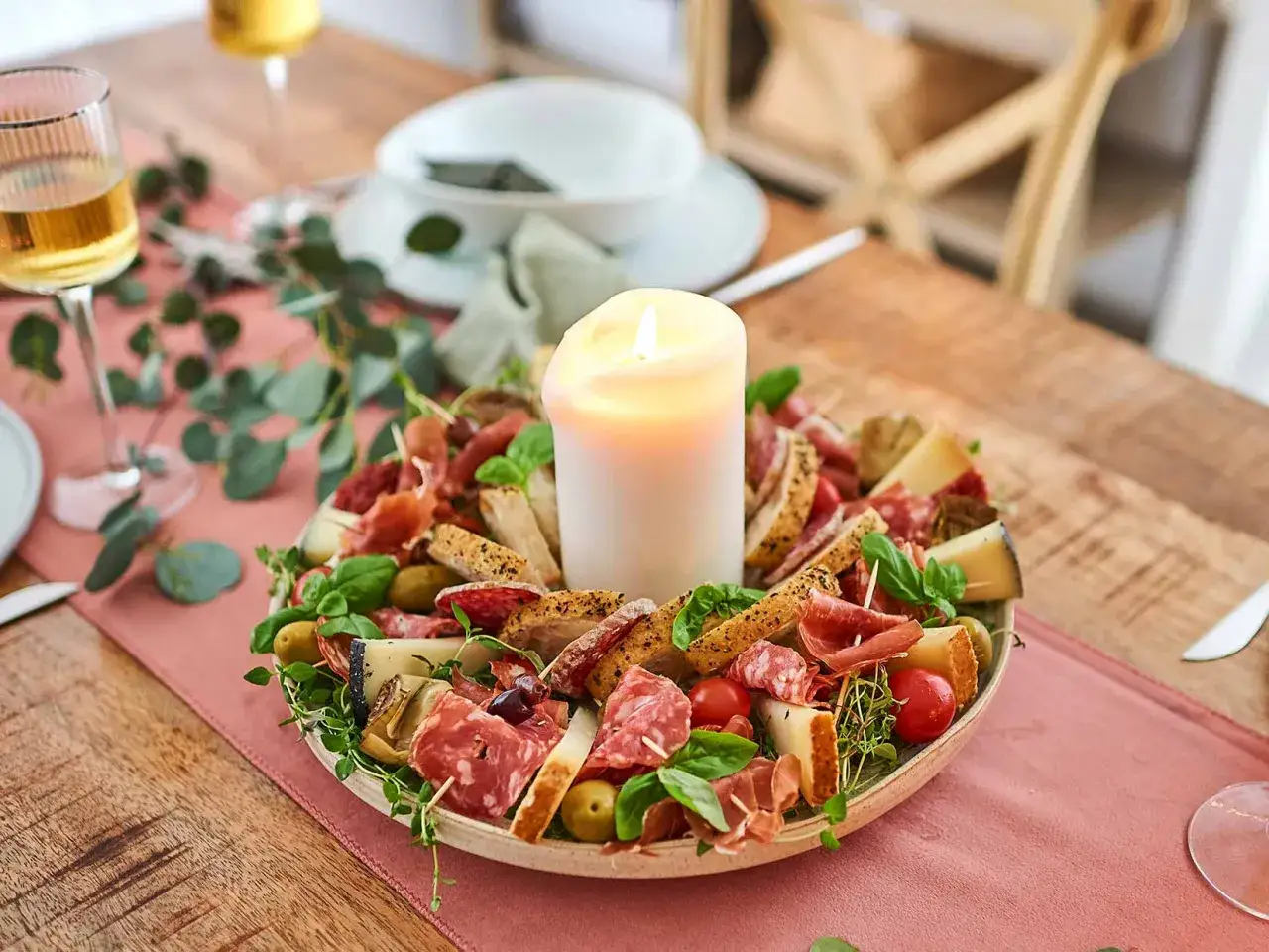 Festliche italienische Crostini mit Wurst, K&auml;se, Oliven und Kr&auml;utern, umgeben von einer Kerze.