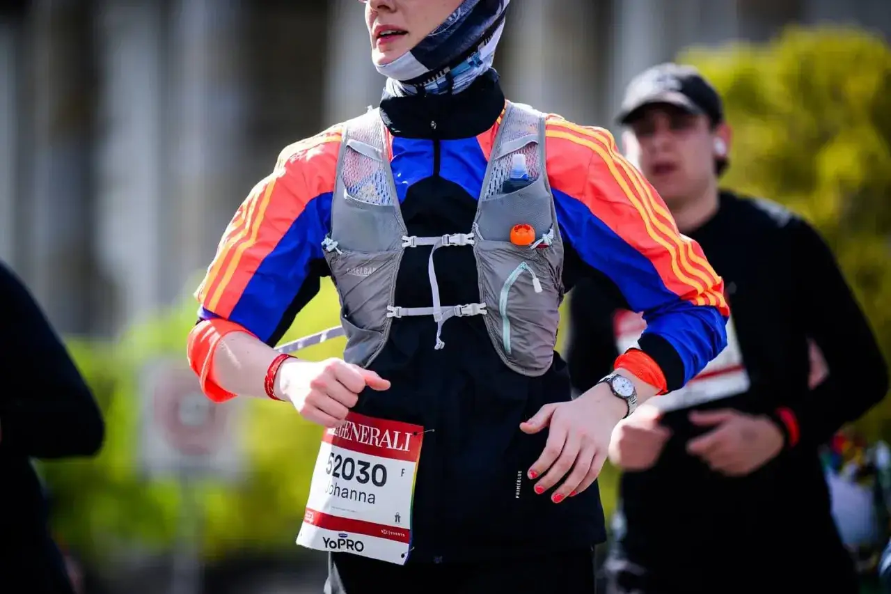 Läuferin mit Startnummer 52030 bei einem Halbmarathon in Essen. Sie trägt eine bunte Laufjacke und eine Trinkweste.