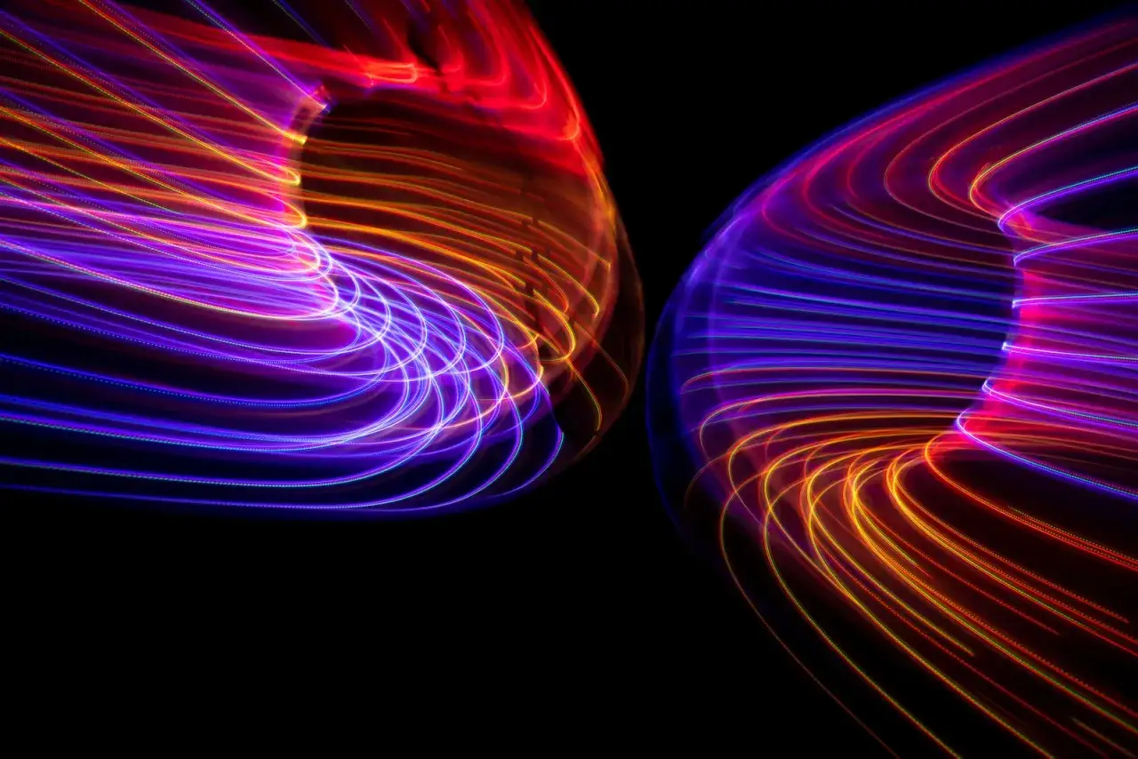 Wirujące światła tworzą ciekawe fotografie. Dwa wiry neonowych barw, fioletu, czerwieni i pomarańczy, na czarnym tle.
