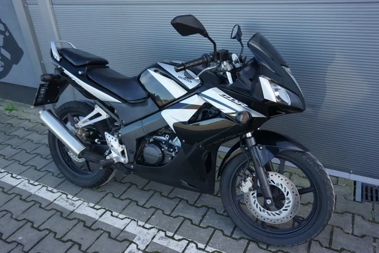 Czarny motocykl Honda CBR z białymi akcentami, zaparkowany na chodniku.
