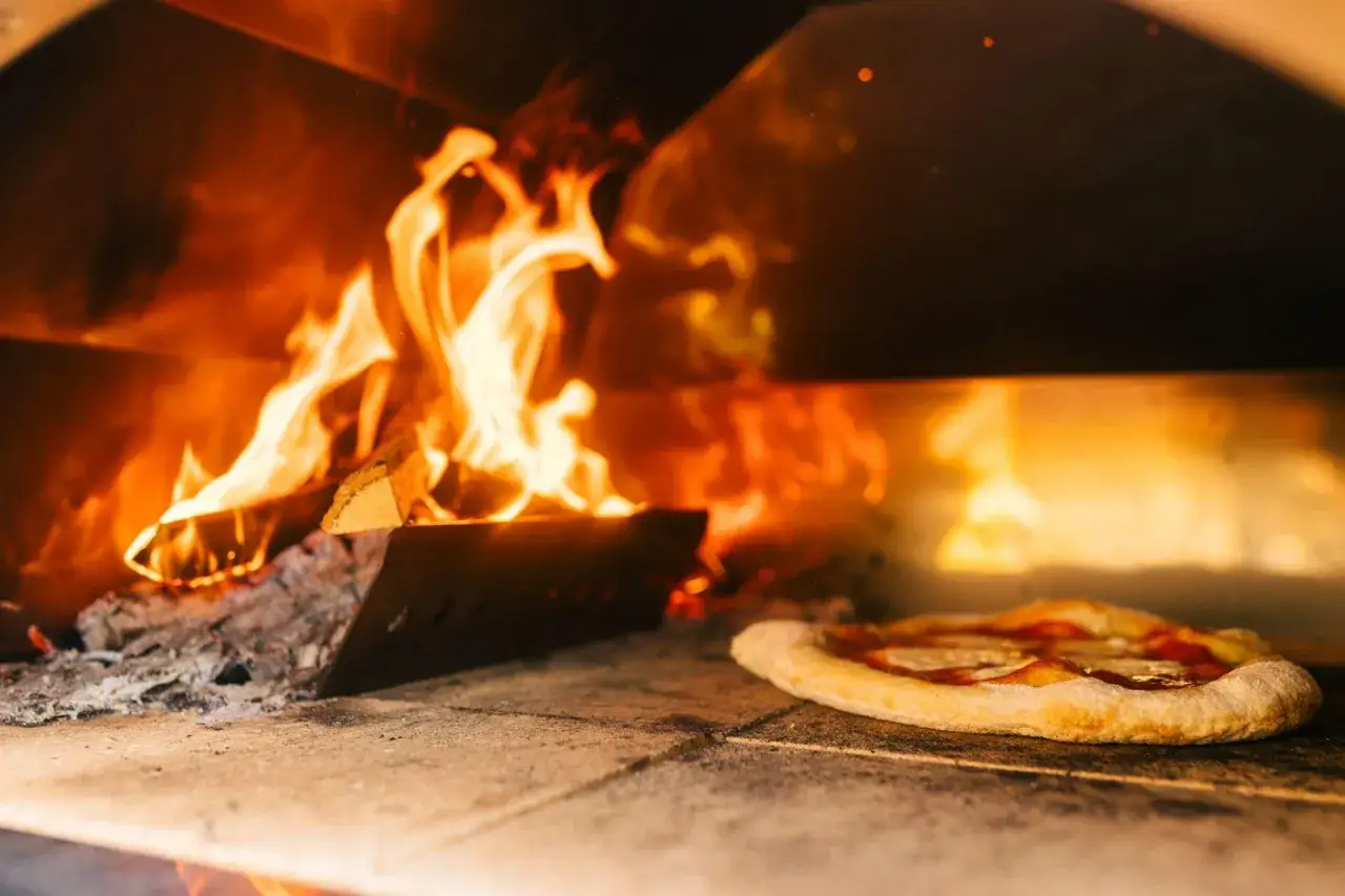 En vedugnsbakad pizza med ost och tomatsås gräddas i en varm ugn med flammande eld.
