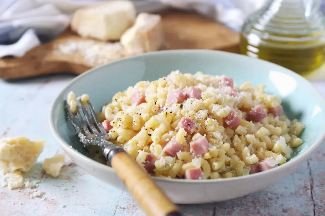Un plat de pâtes simple et savoureux, parfait pour une recette rapide. Des dés de jambon, du fromage râpé et du poivre noir sur des macaronis.