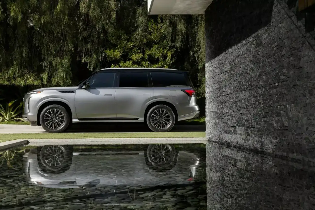 El Infiniti QX80, con su elegante diseño plateado, se refleja en el agua. Descubre el infiniti qx80 precio españa.
