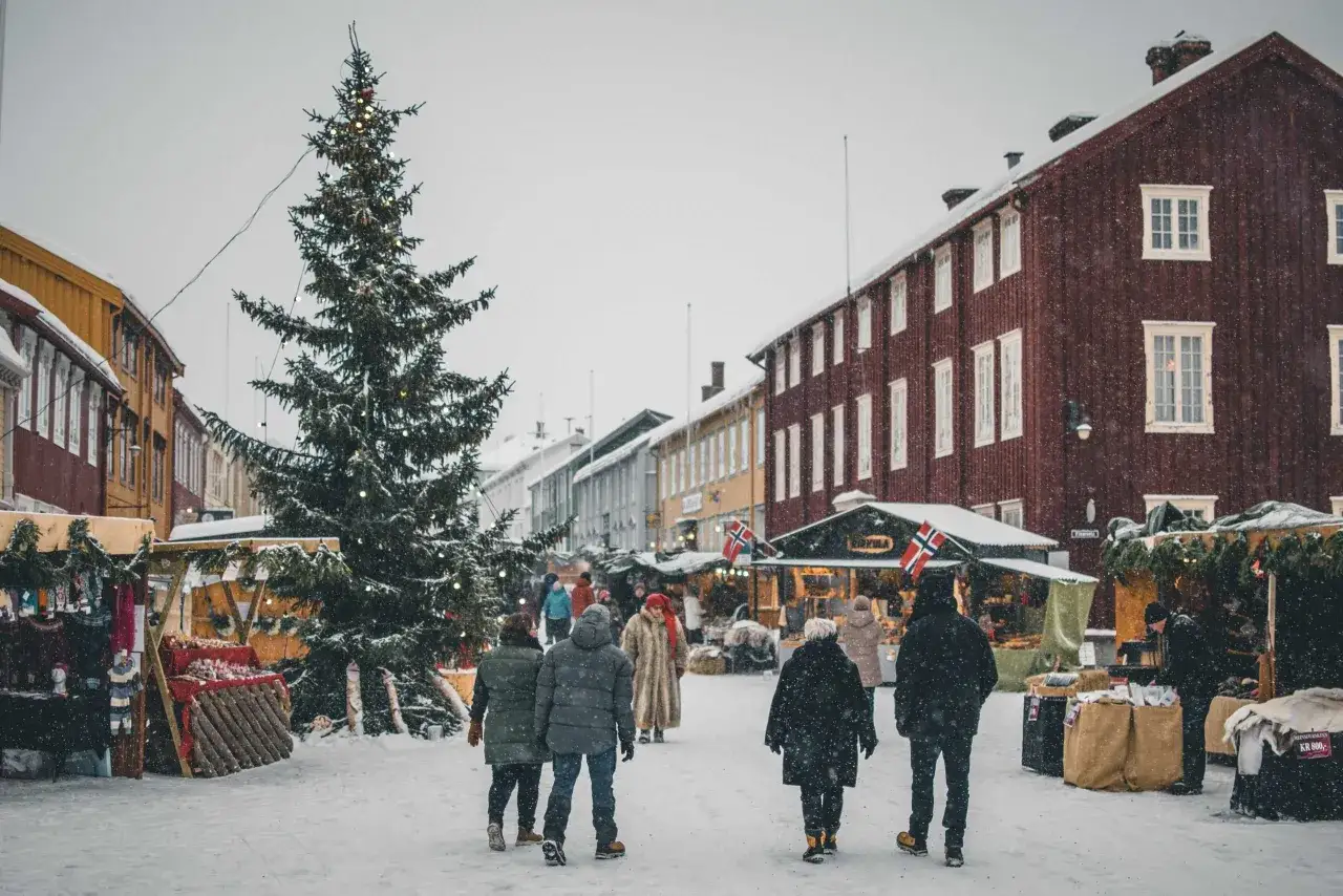 Święta w Norwegii: zimowy jarmark w zaśnieżonym miasteczku, ozdobiona choinka i ludzie spacerujący między straganami.